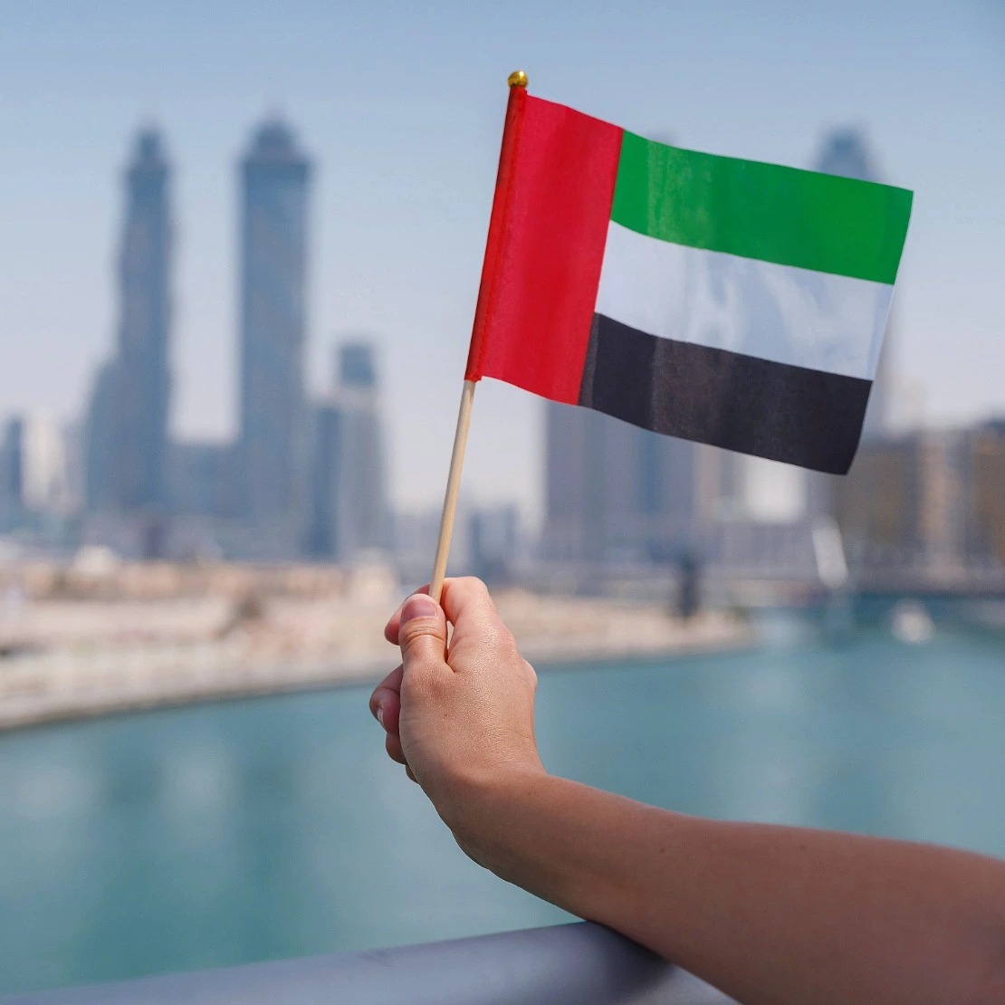 Hand holding UAE flag with iconic Dubai skyline representing new beginnings, business opportunities, and successful company setup in the UAE for Europeans and Indian entrepreneurs - EL Business Consultants