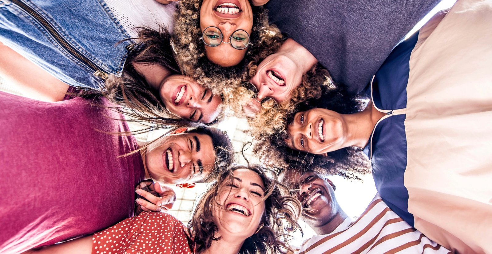 A diverse group of joyful family members standing in a circle and looking down at the camera with big smiles, showcasing successful family reunification.